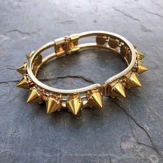 This stunning cuff is made of individually handset gold spikes in pronged settings, arranged around a hinge closure cuff. The oval shape fits comfortably on most wrists and is perfect for stacking or wearing solo. With its edgy design, this cuff will add a touch of rebellious glamour to any outfit. Whether you're dressing up for a night out or adding a little edge to your everyday look, the Helios Cuff is the perfect accessory for any occasion. DETAILS Bracelet Diameter: 7” Punk Style Gold Metal Bracelet, Gold Punk Style Metal Bracelet, Edgy Spiked Jewelry For Parties, Gold Metal Punk Bracelets, Gold Metal Punk Bracelet, Punk Metal Bangle Cuff Bracelet, Punk Style Metal Cuff Bangle Bracelet, Adjustable Spiked Metal Jewelry, Adjustable Metal Jewelry With Spikes