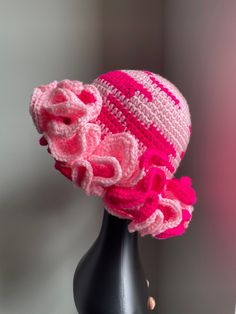 a crocheted pink hat with ruffles on top sitting on a mannequin head