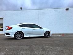 a white car is parked in front of a building with a brick wall behind it