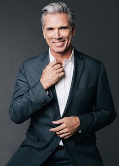 a man in a black suit and white shirt is posing with his hands on his chest