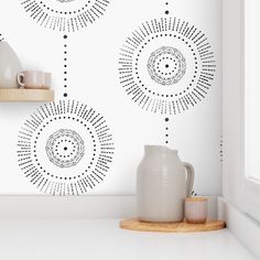 a white vase sitting on top of a counter next to a wall with black dots