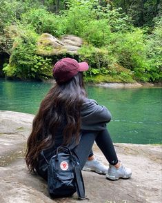 a woman sitting on top of a rock next to a river