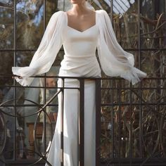 a woman is standing on a fence wearing a white dress with long sleeves and an open back