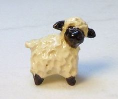 a small toy sheep standing on a white surface with its head turned to the side