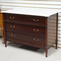 an antique dresser with white marble top and brass handles in front of a striped wall