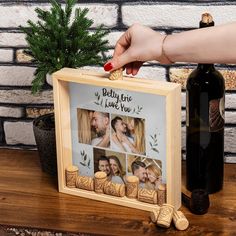 a person holding a wooden frame with photos on it next to a bottle of wine