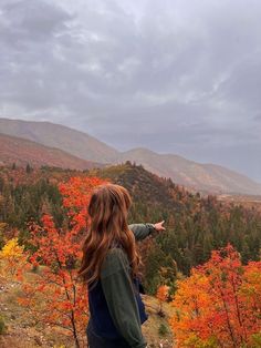 a woman standing on top of a hill pointing at the trees that are changing colors