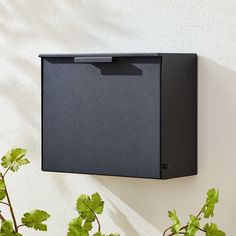 a black box mounted to the side of a white wall next to a potted plant