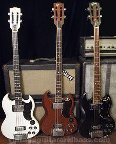 three guitars are lined up next to each other on a table in front of amps