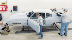 two men working on an old car in a garage with another man looking at it