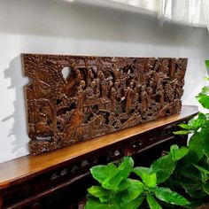 a carved wooden panel sitting on top of a table next to a potted plant