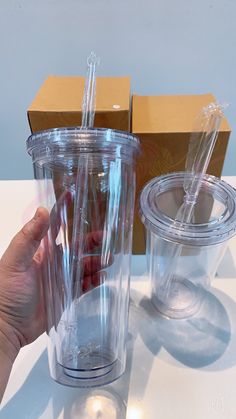 a hand holding a plastic cup next to a cardboard box with two straws in it