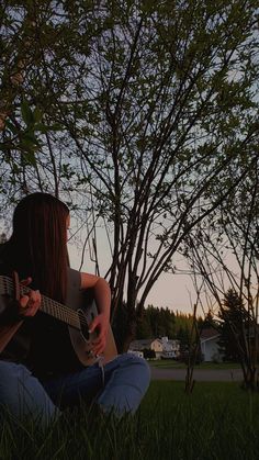 a woman sitting in the grass playing an acoustic guitar