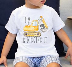 a little boy sitting on top of a couch wearing a construction themed t - shirt