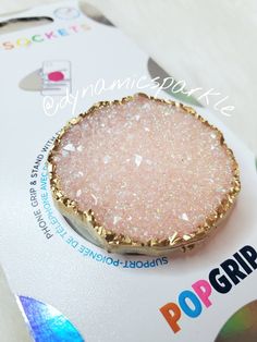 a pink and gold glittered brooch sitting on top of a white card board