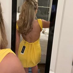 a woman in a yellow dress looking at herself in the mirror with her back to the camera