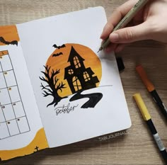 a hand holding a pen and drawing a halloween scene in an open notebook with the calendar on it