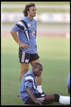 two soccer players sitting on the ground during a game, one with his foot on the ground