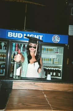 a woman wearing a hat and holding a drink in front of a bud light store