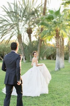 a bride and groom walking through the grass in front of palm trees at their wedding