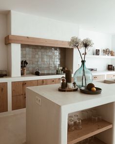 a vase with flowers on top of a counter in a kitchen next to some glasses