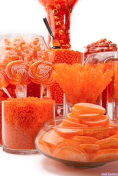 an assortment of candies and candy in glass bowls on a table with orange decorations