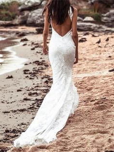 a woman is walking on the beach in a white wedding dress with open back and long train