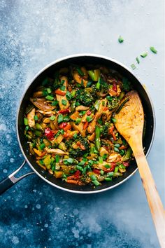 a pan filled with stir fry vegetables on top of a blue countertop next to a wooden spoon