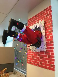 a man dressed as santa claus hanging from a brick wall with christmas lights on it