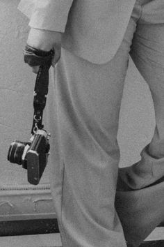 black and white photograph of man in suit with camera attached to his leg while standing on tiled floor