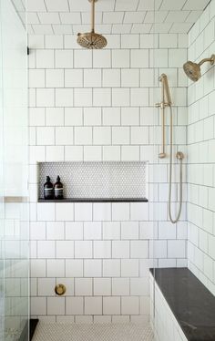 a white tiled bathroom with black counter tops and gold faucet shower head in the corner