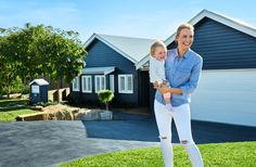 a woman holding a small child in front of a blue house with white shutters