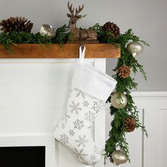 a christmas stocking hanging from a mantel with pine cones and silver baubes