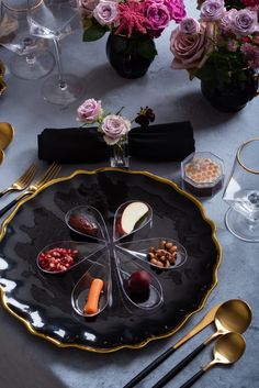 a black plate with gold trim and spoons on it, surrounded by silverware