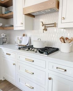 a kitchen with white cabinets and gold pulls on the stove top, along with wooden utensils