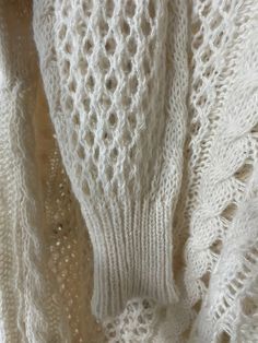 a white knitted sweater with holes in the middle and an openwork design on it