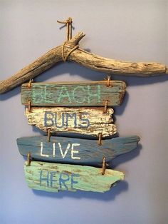 three wooden signs hanging on a wall next to driftwood sticks with words that read beach bums live here