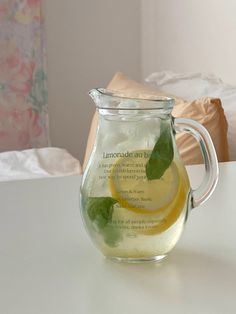 a glass pitcher filled with lemonade sits on a white table next to a pillow