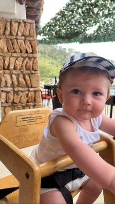 a baby sitting in a wooden chair with a hat on top of it's head