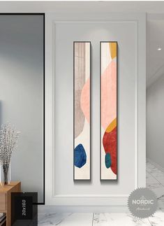 two abstract paintings on the wall next to a vase with flowers in it and an open door