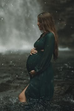 a pregnant woman standing in the water with her hands on her belly, wearing a green dress