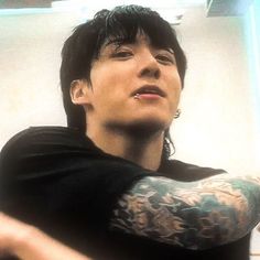 a man with black hair and tattoos holding a cell phone in his right hand while looking up at the sky