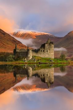 a castle sitting on top of a lake surrounded by mountains