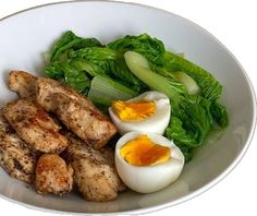 a white bowl filled with meat and eggs next to lettuce on the side