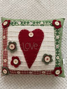 a red heart on a green and white pillow that says love with buttons attached to it