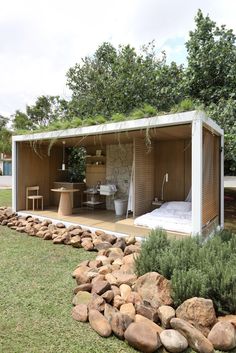 an outdoor room with a bed and desk in the center surrounded by rocks, grass and trees