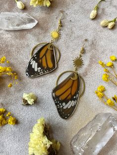 three butterfly earrings sitting on top of a table next to flowers and ice cubes