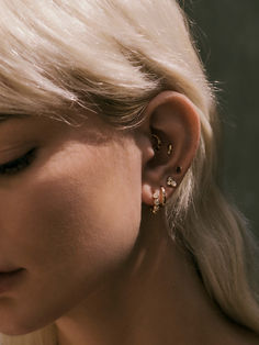 a woman with blonde hair is wearing gold ear cuffs and has her face close to the camera