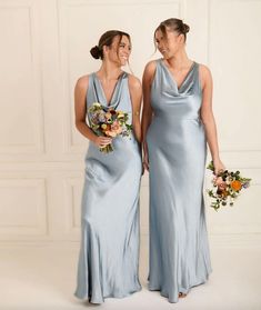 two women in blue dresses standing next to each other holding bouquets and smiling at the camera