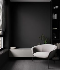 a white chair sitting in front of a window next to a book shelf with books on it